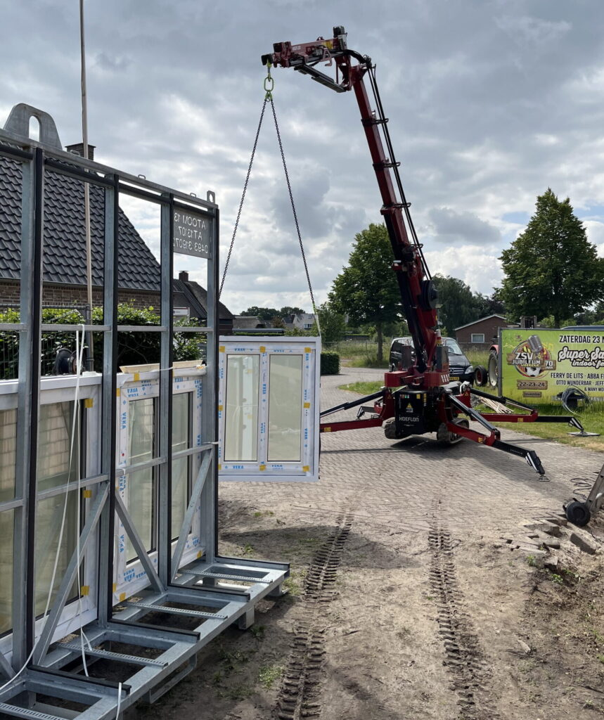 Een kleine hijskraan die een prefab kozijn van een stalen bok af hijst.